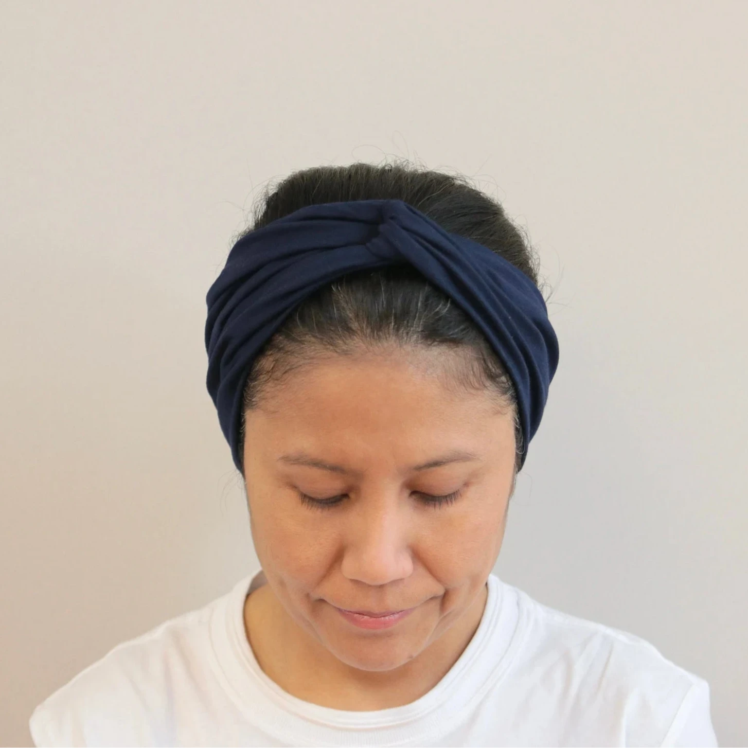 Woman wearing a navy blue headband against a beige background