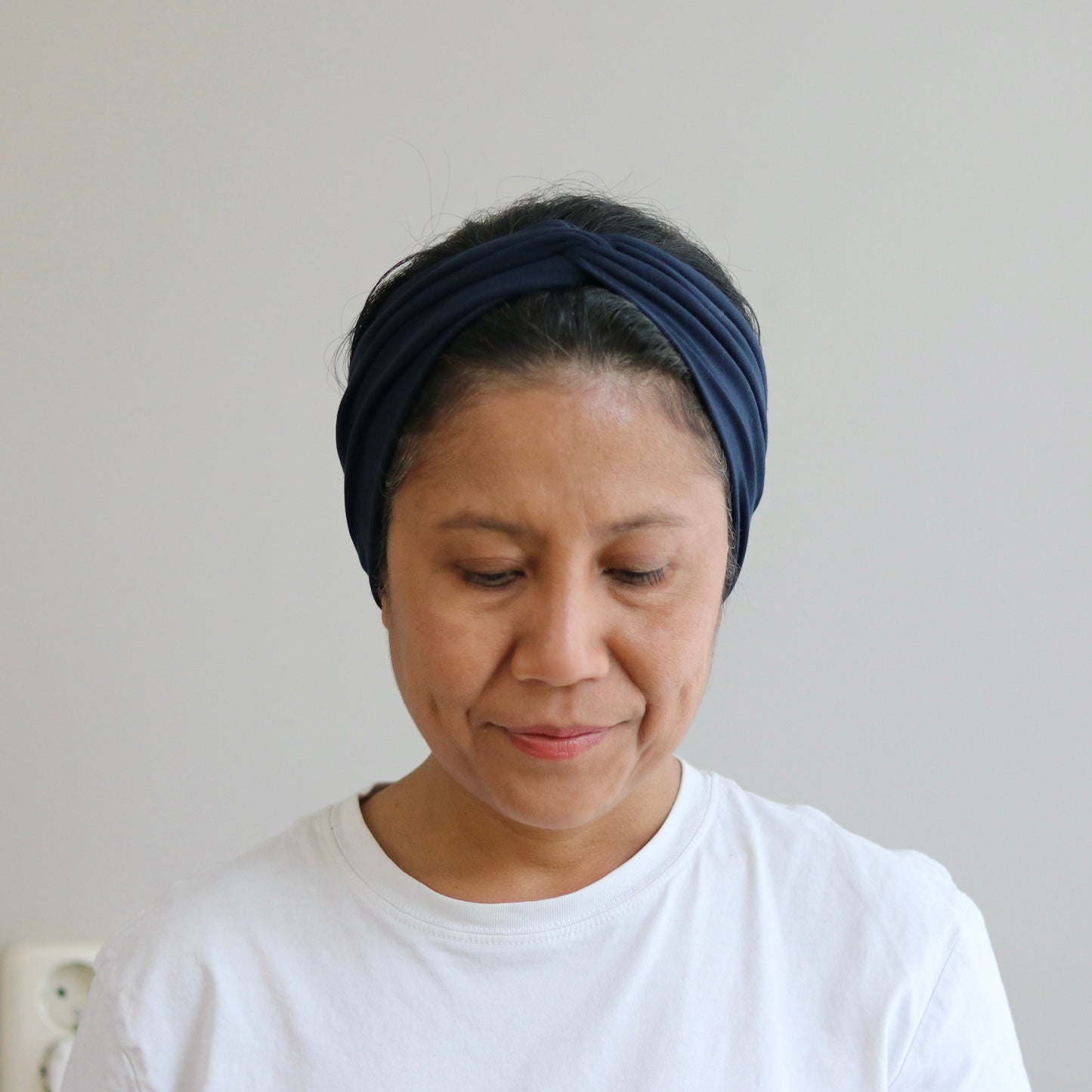 Woman wearing a blue headband and white shirt against a plain background