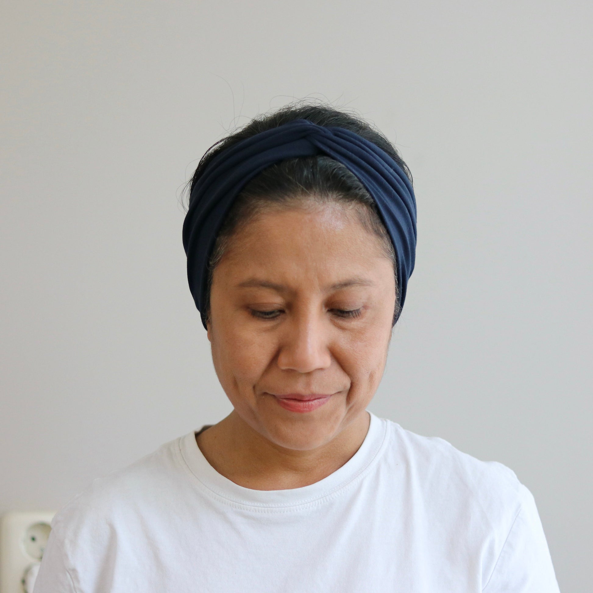 Woman wearing a blue headband and white shirt against a plain background