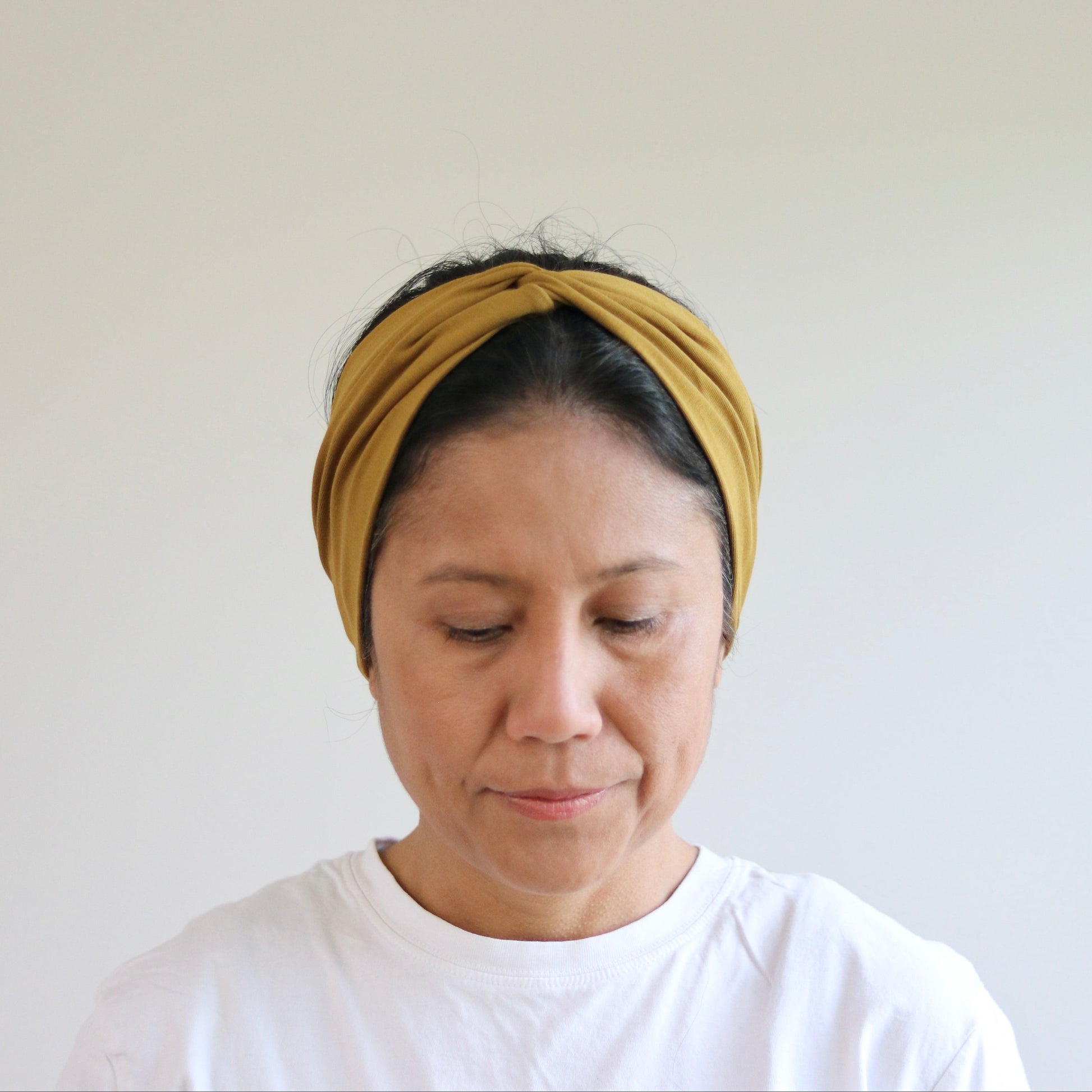 Person wearing an ocher- brown headband against a white background