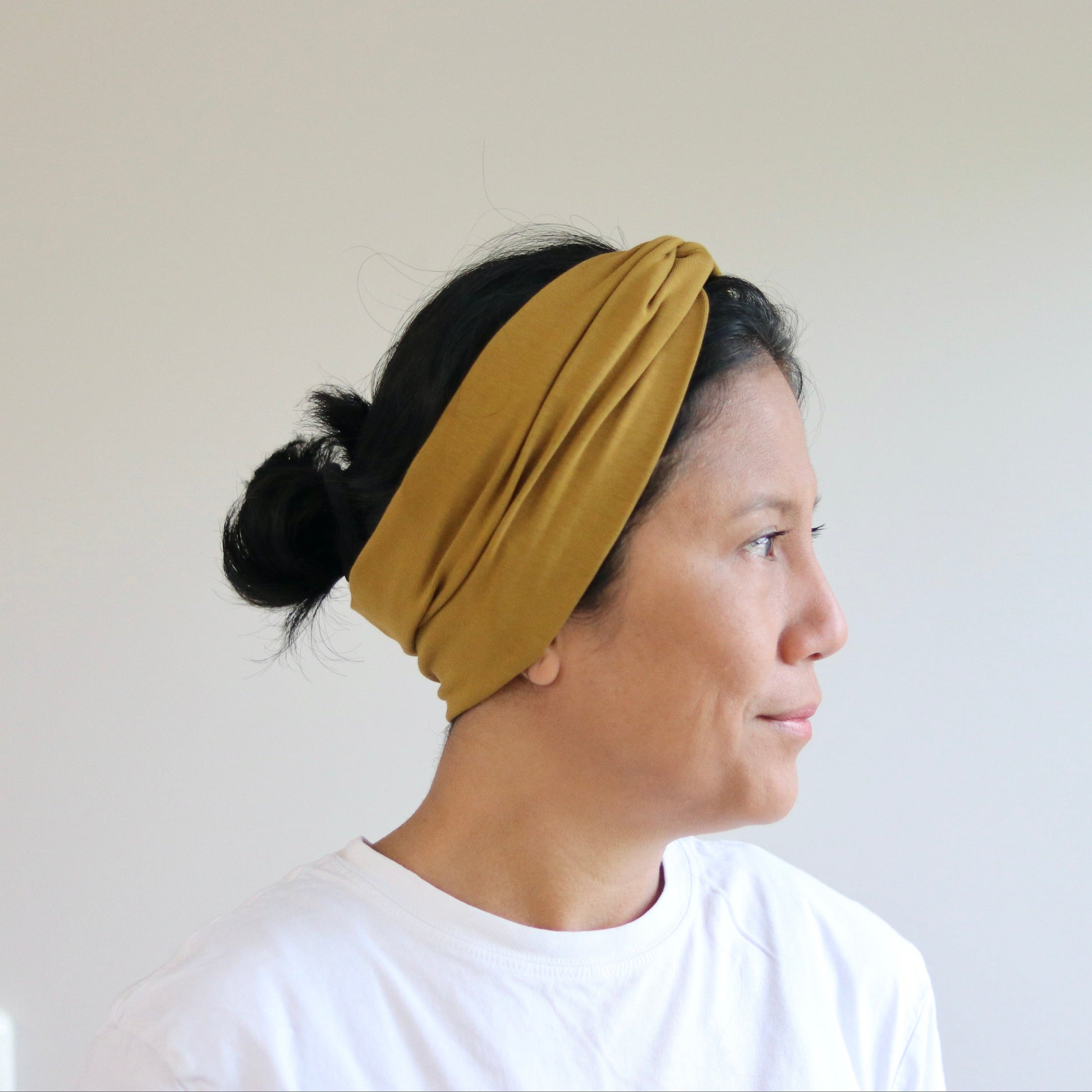 Woman wearing a mustard yellow headband against a plain background
