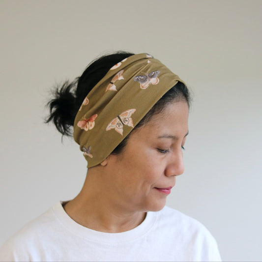 Woman wearing a moss green headband with floral pattern against a plain background