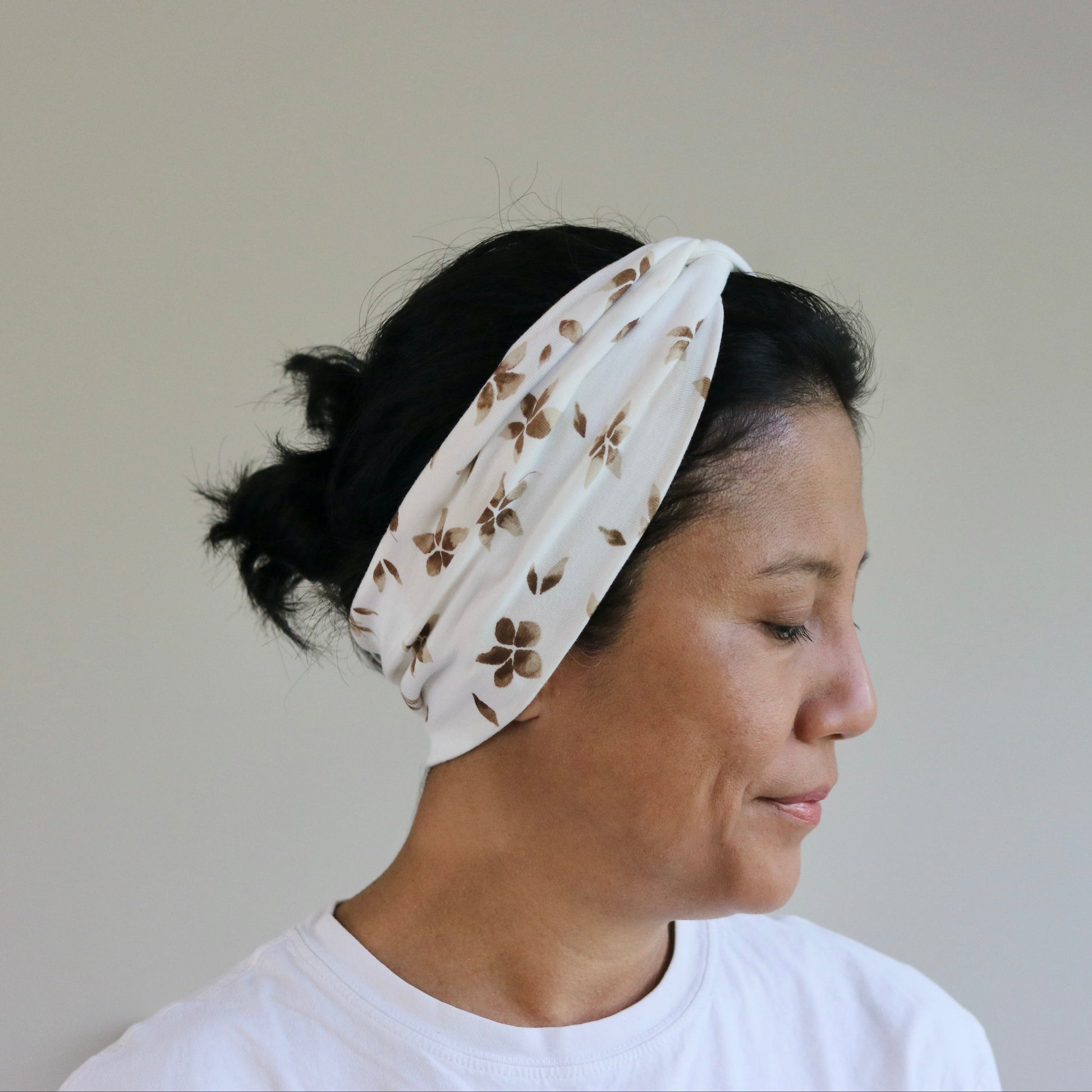 Woman wearing a white headband with floral pattern against a plain background