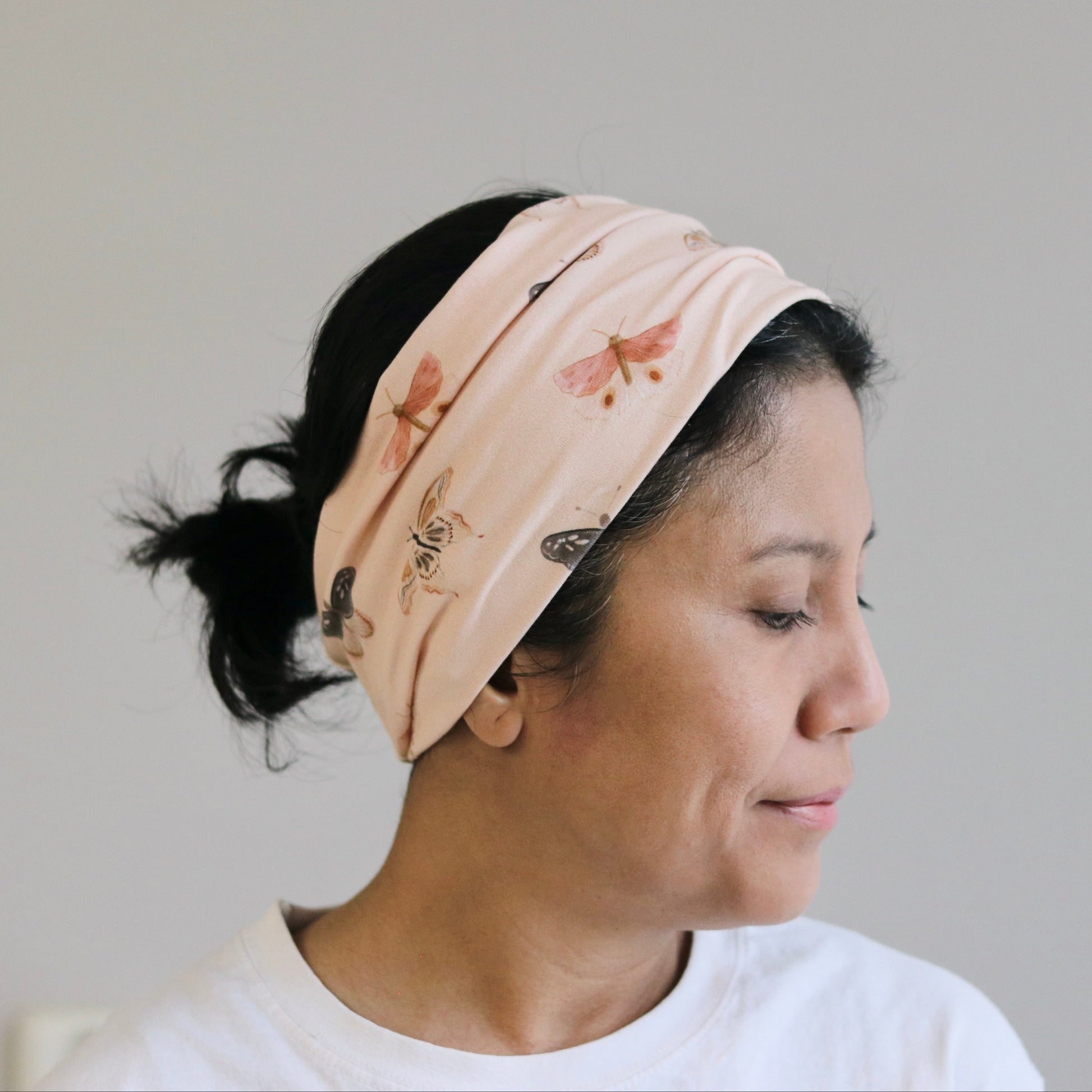 Woman wearing a beige headband with floral patterns against a plain background