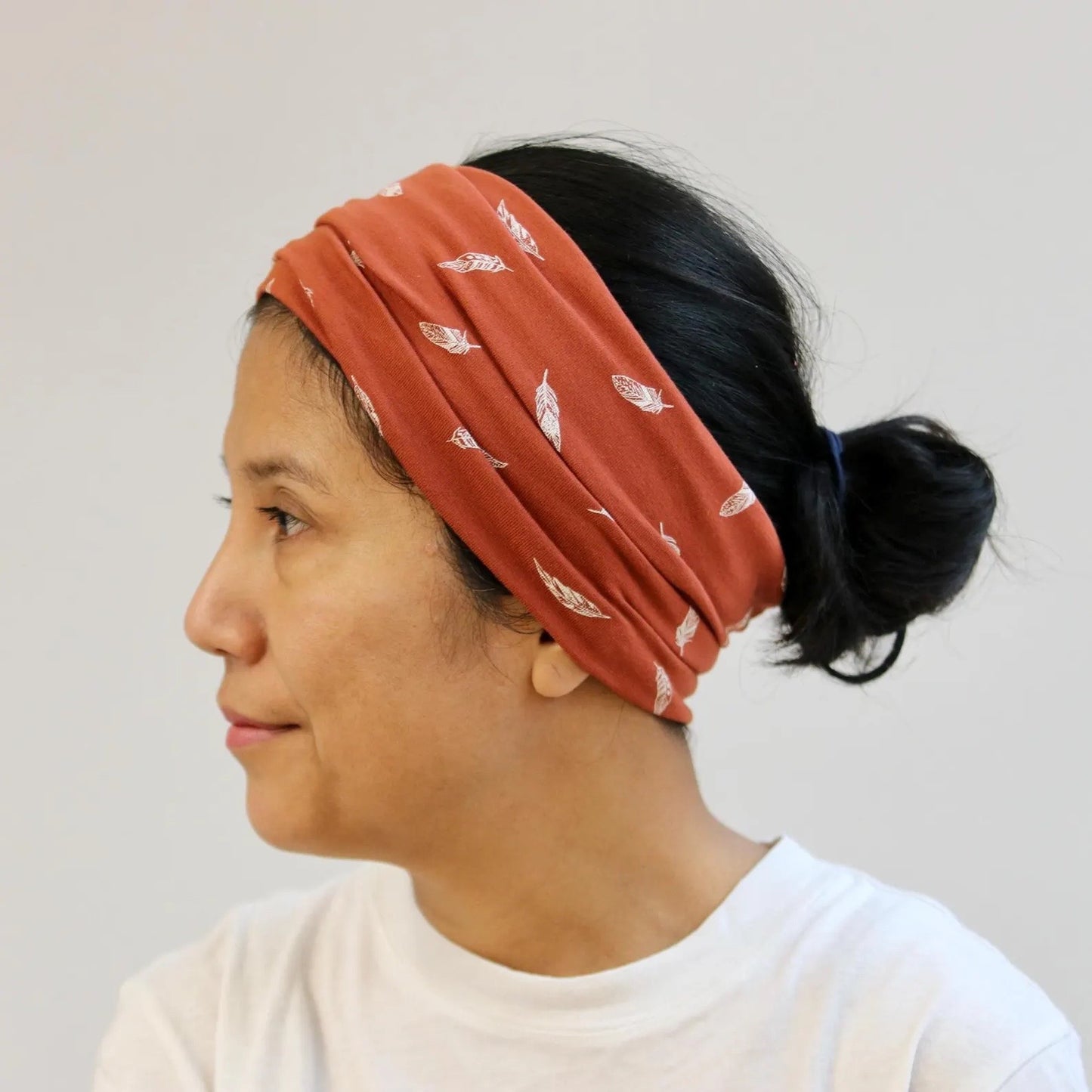 Woman wearing a rust-colored headband with feather pattern on a plain background