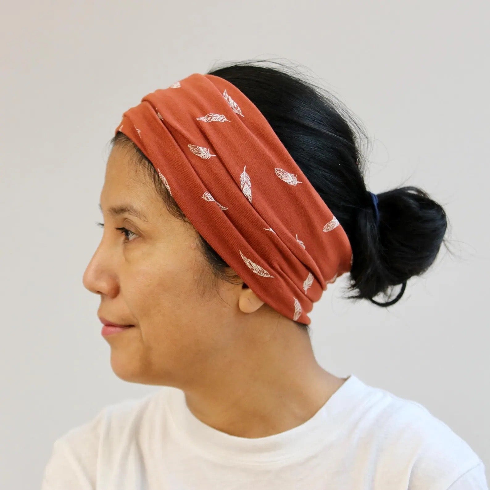 Woman wearing a rust-colored headband with feather pattern on a plain background