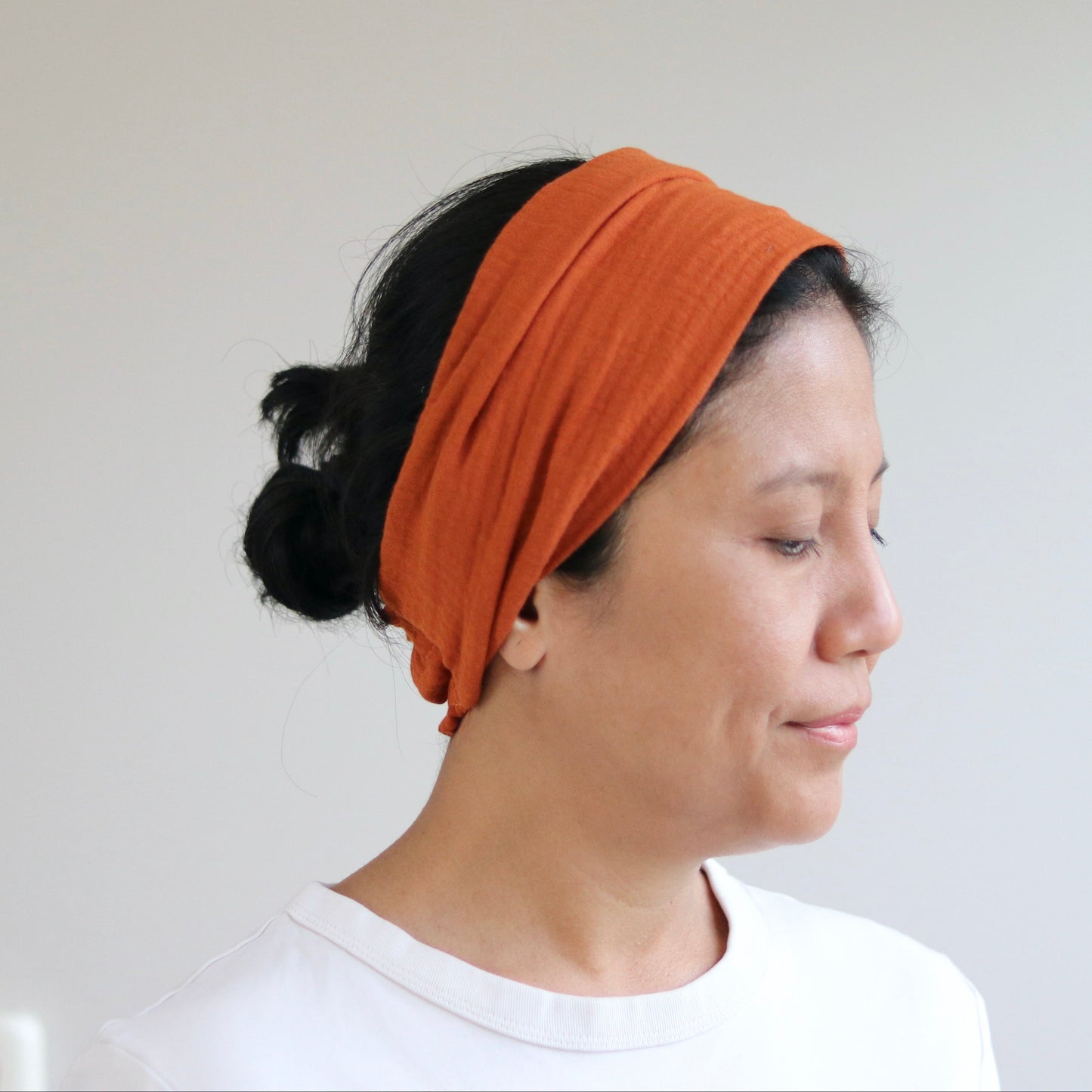 A woman wearing a wide terra headband and a white t-shirt, shown in profile against a plain light gray wall.
