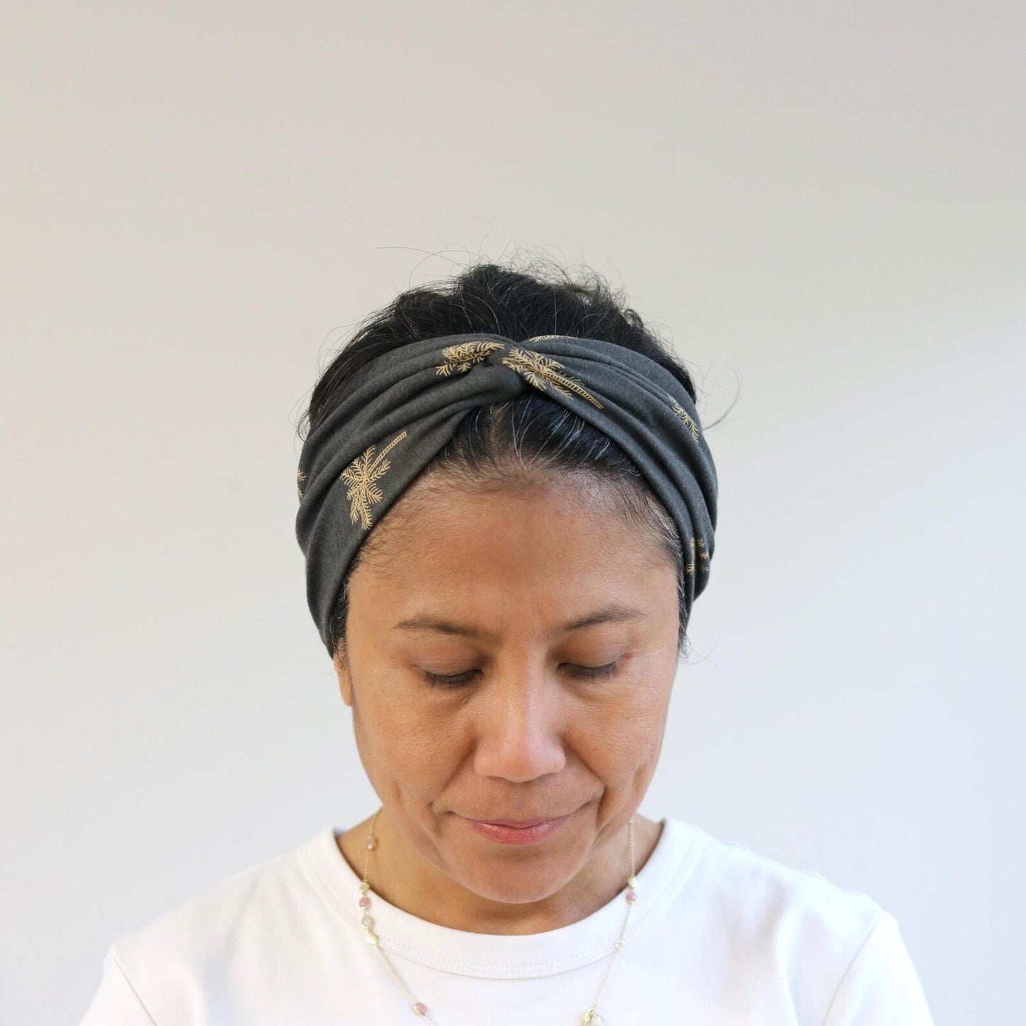 Woman wearing a gray headband with gold accents against a white background