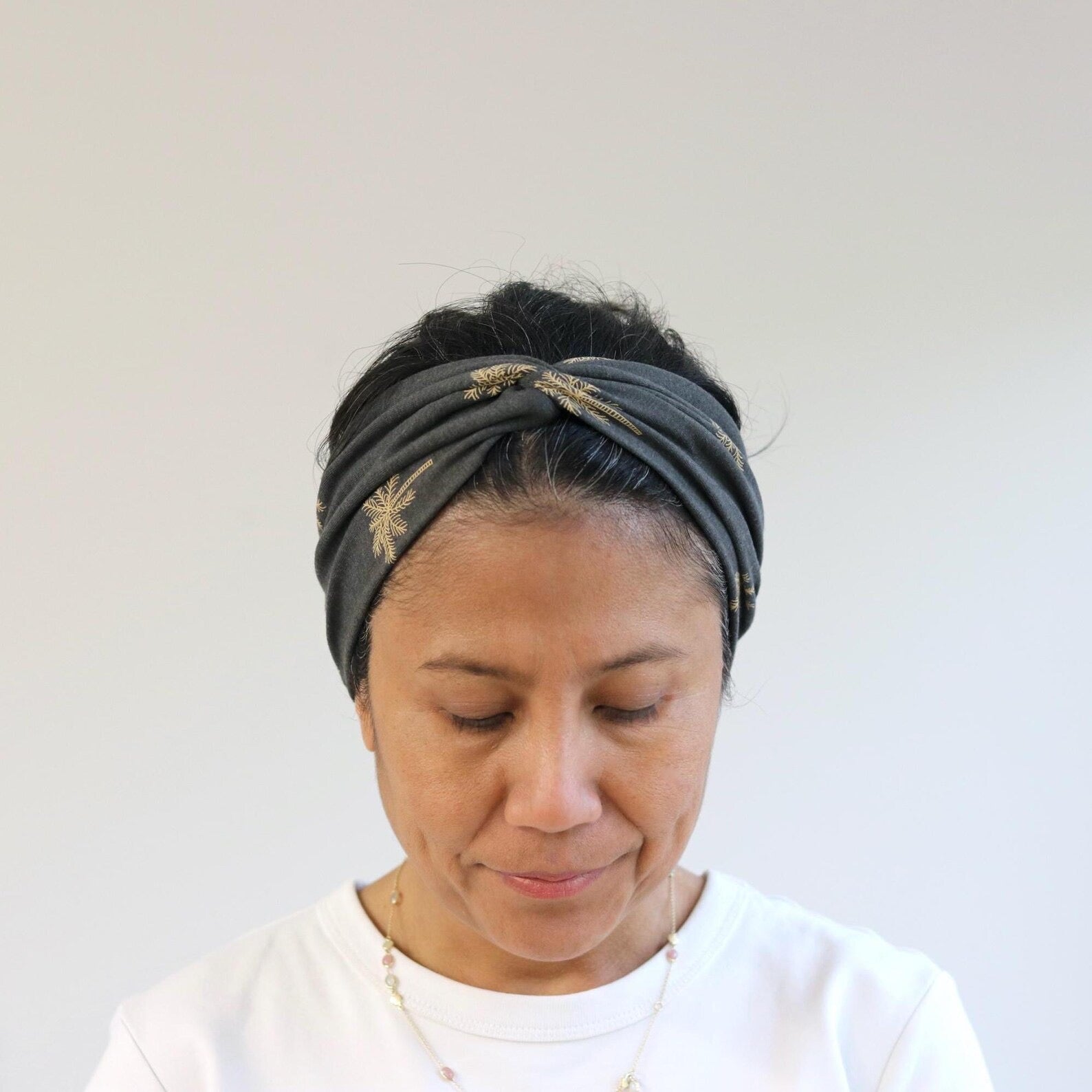 Woman wearing a gray headband with gold accents against a white background