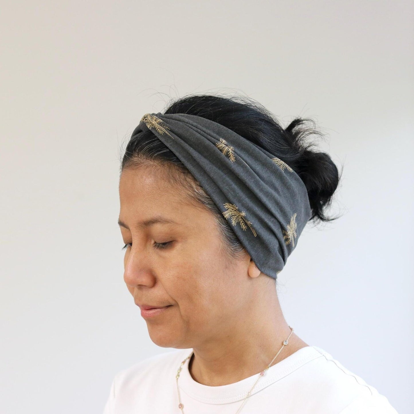 Woman wearing a gray headband with gold accents on a plain background