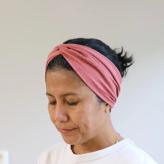 Woman wearing a red- melange knotted headband against a plain background