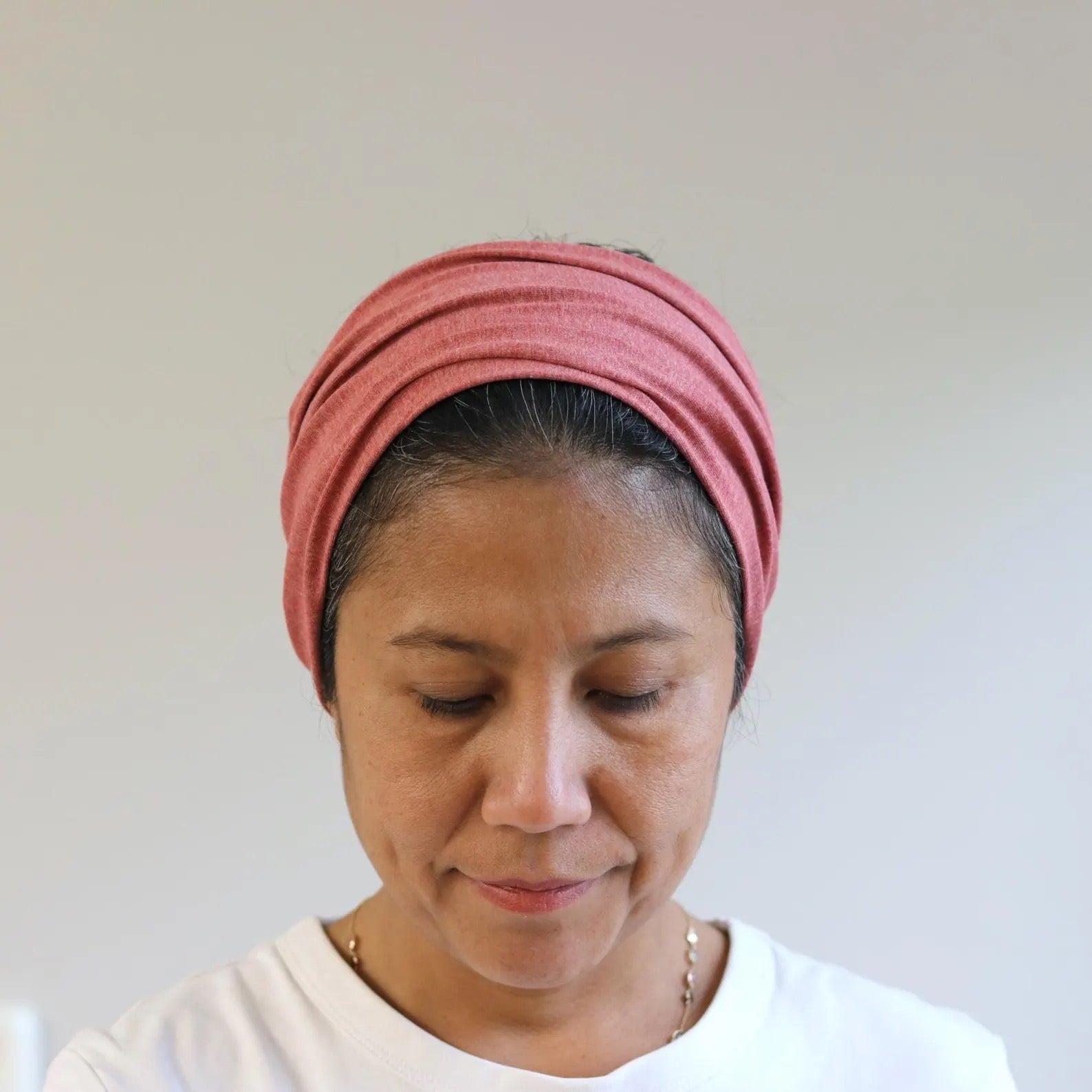 Woman wearing a red- melange headscarf against a plain background