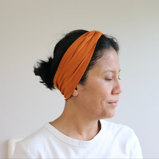 Woman wearing an orange headband against a plain background