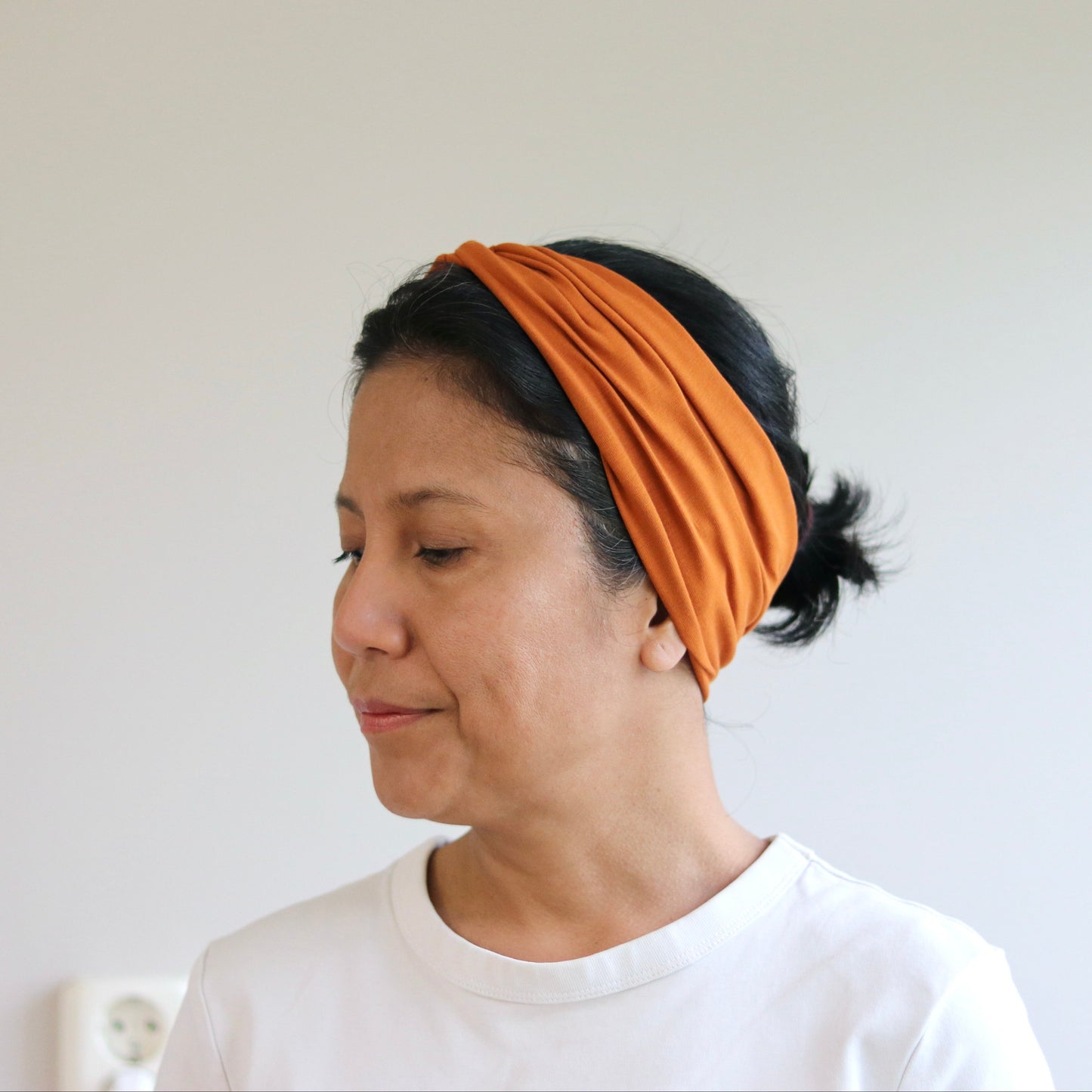 Woman wearing an orange headband against a plain background