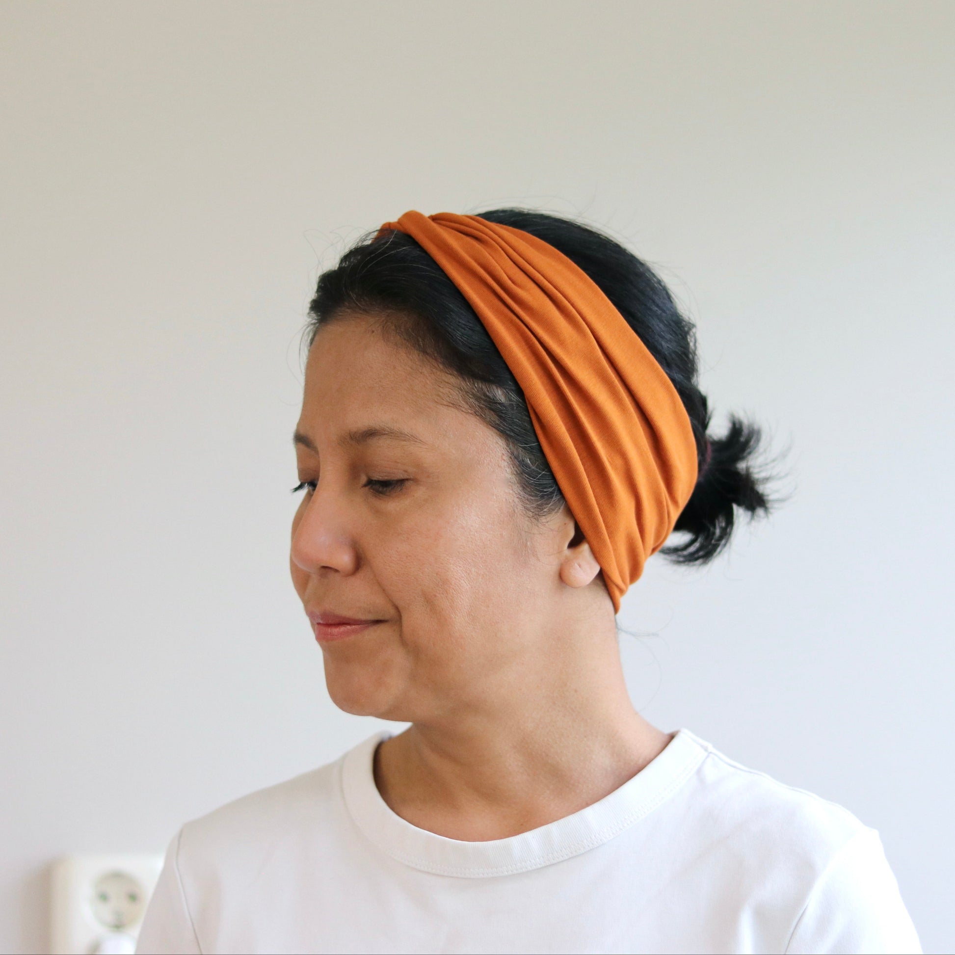 Woman wearing an orange headband against a plain background