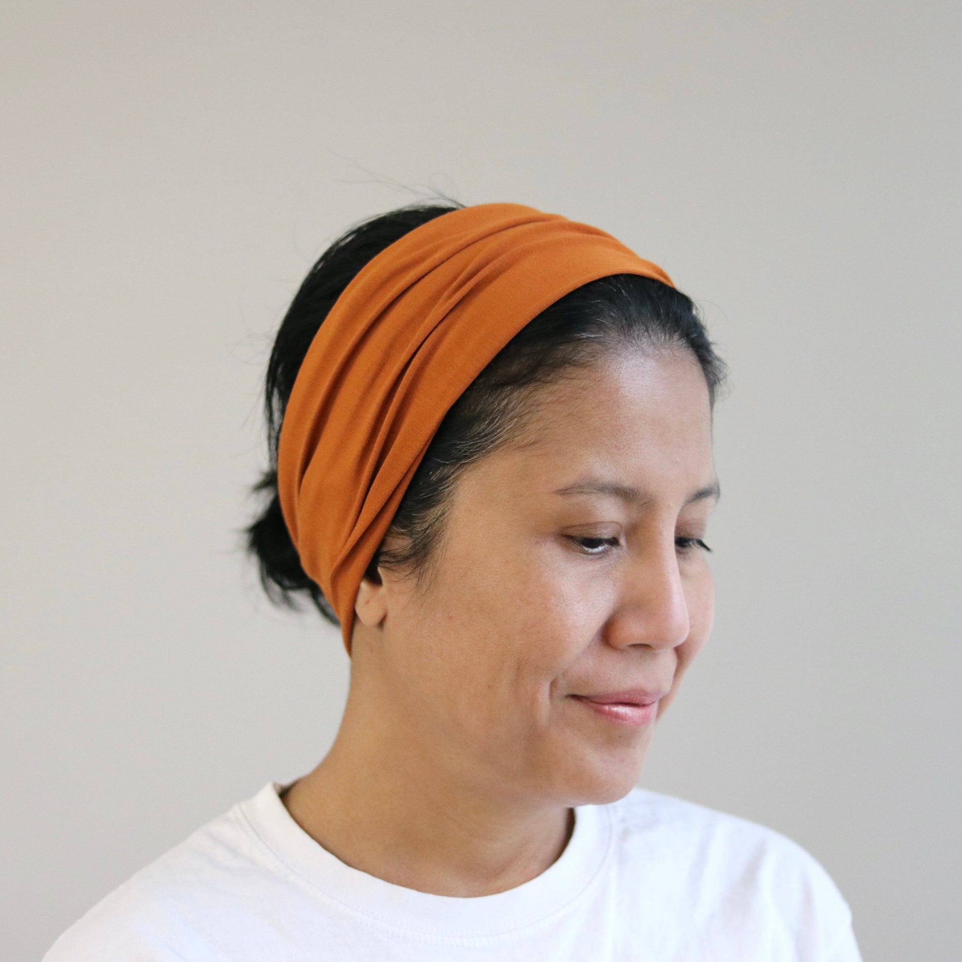 Woman wearing an orange headband against a plain background