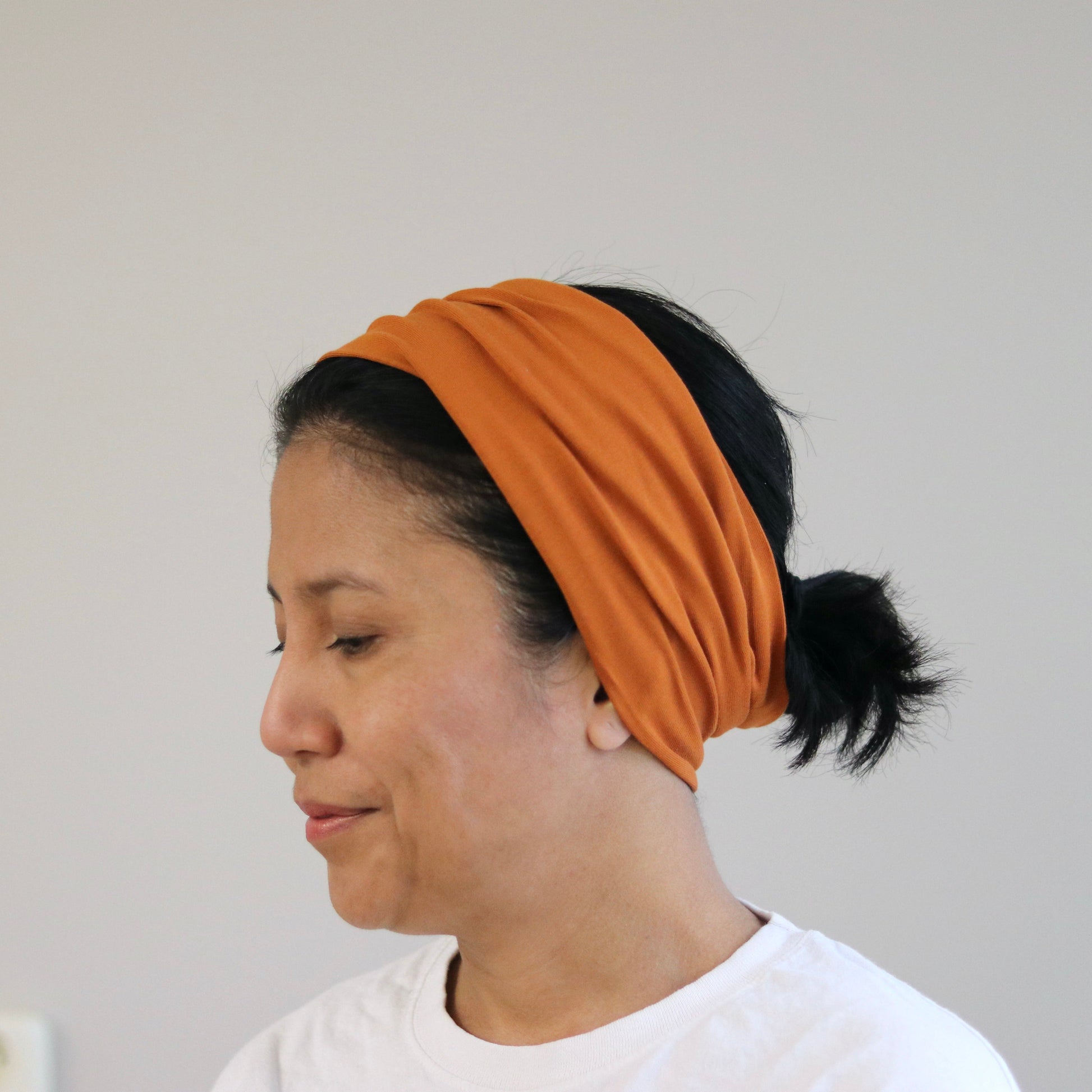 Woman wearing a rust- orange headband against a plain background