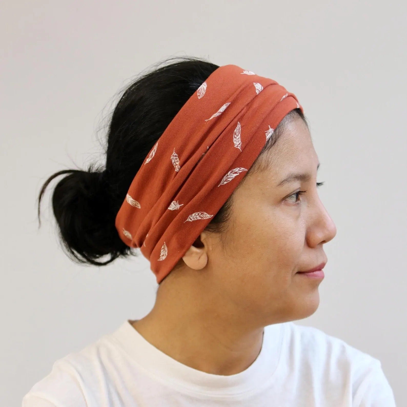 Person wearing a rust-colored headband with feather pattern on a plain background