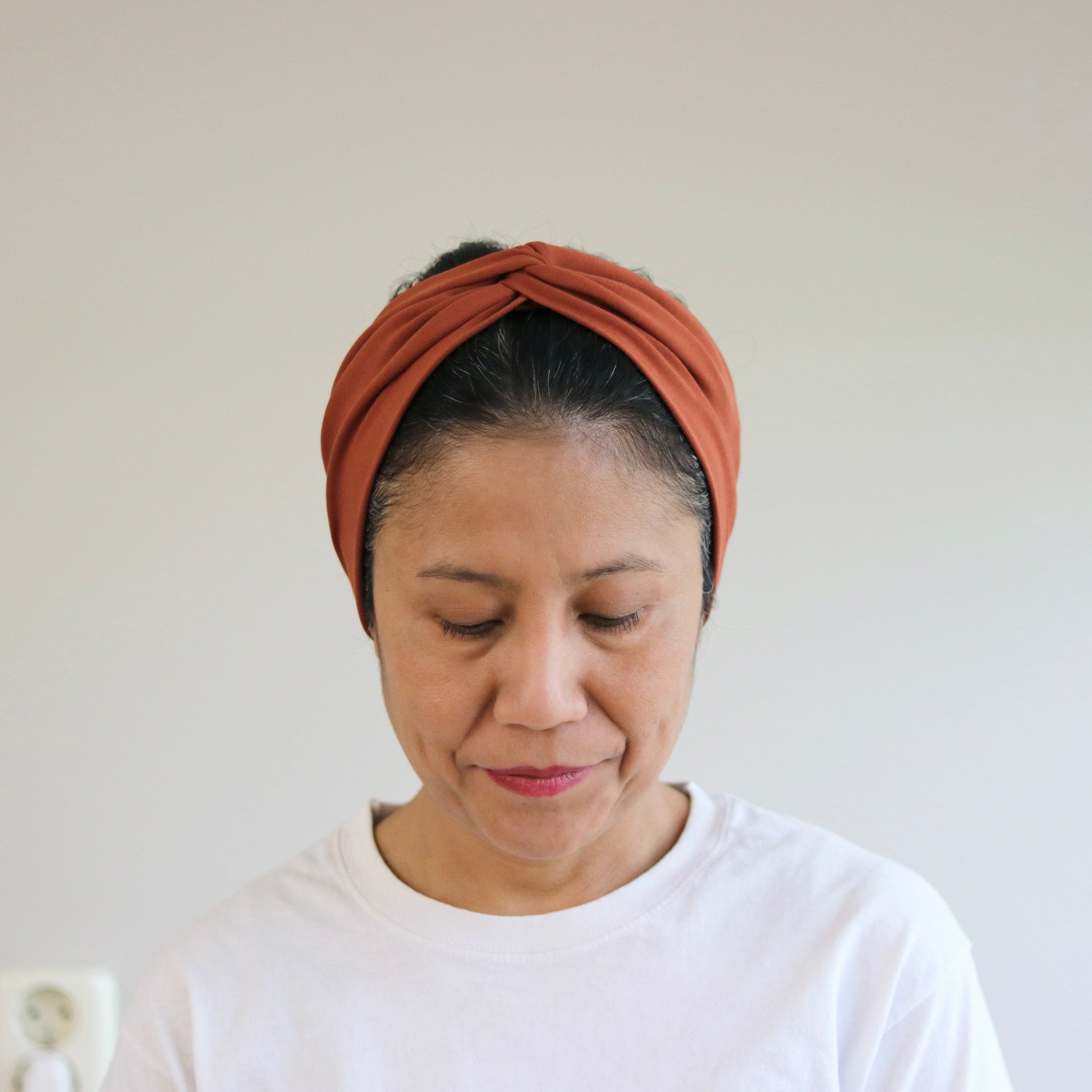 Woman wearing a rust-colored headband against a plain background