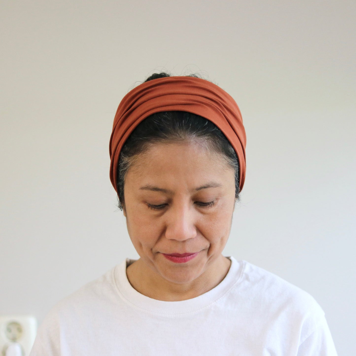 Woman wearing a rust-colored headband against a plain background