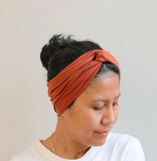 Woman wearing a rust-colored headband against a plain background