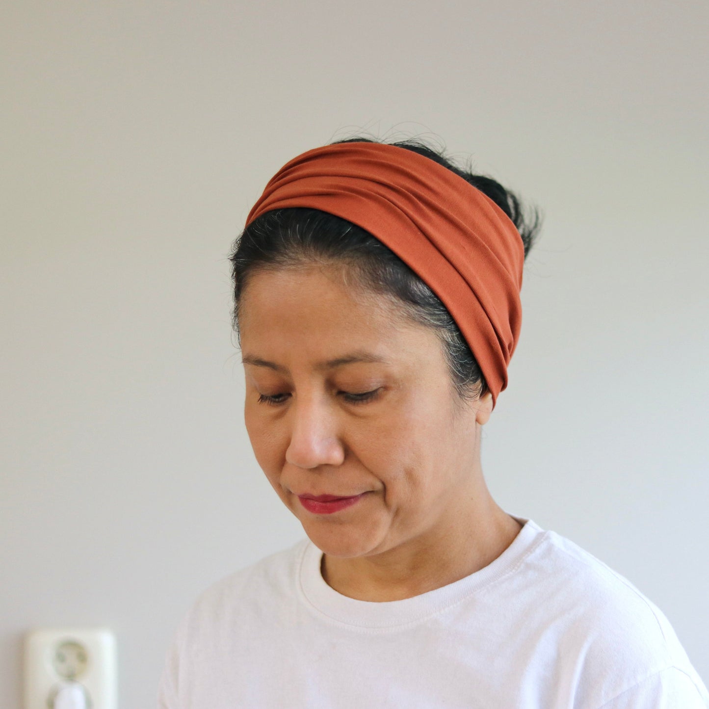 Woman wearing a rust-colored headband against a plain background