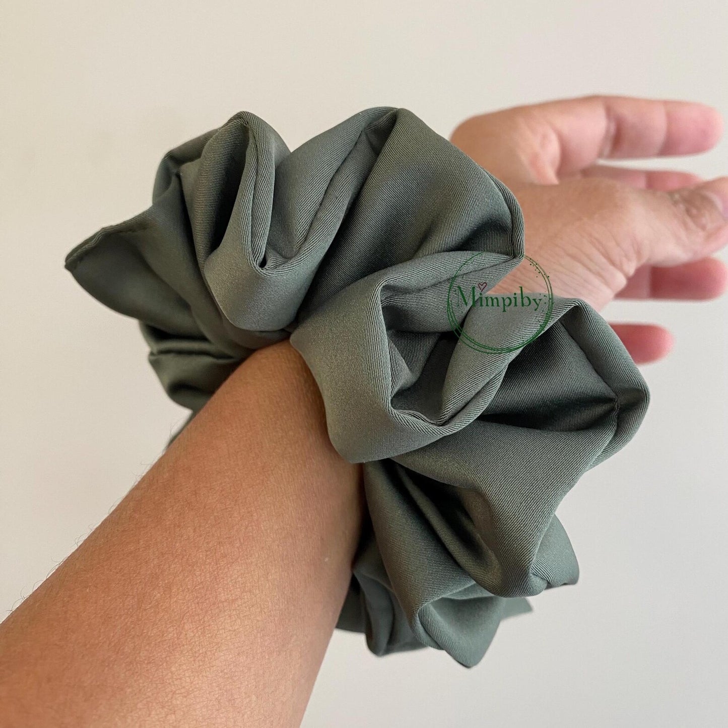 Person wearing a green scrunchie on wrist with a plain background