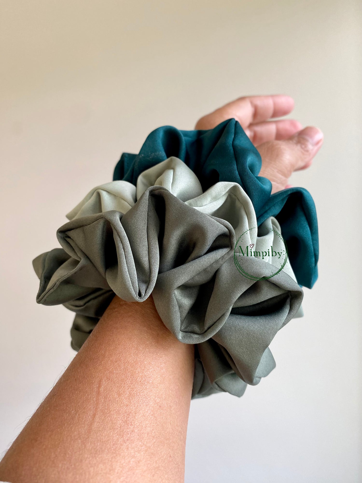 Hand wearing a stack of three scrunchies on a plain background