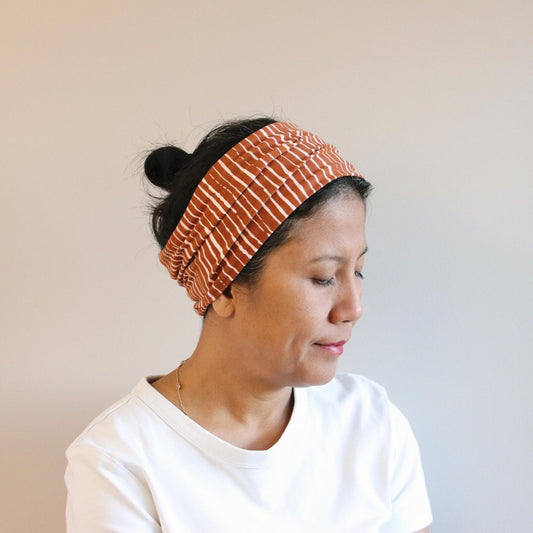 Woman wearing a rust-colored patterned headband against a neutral background