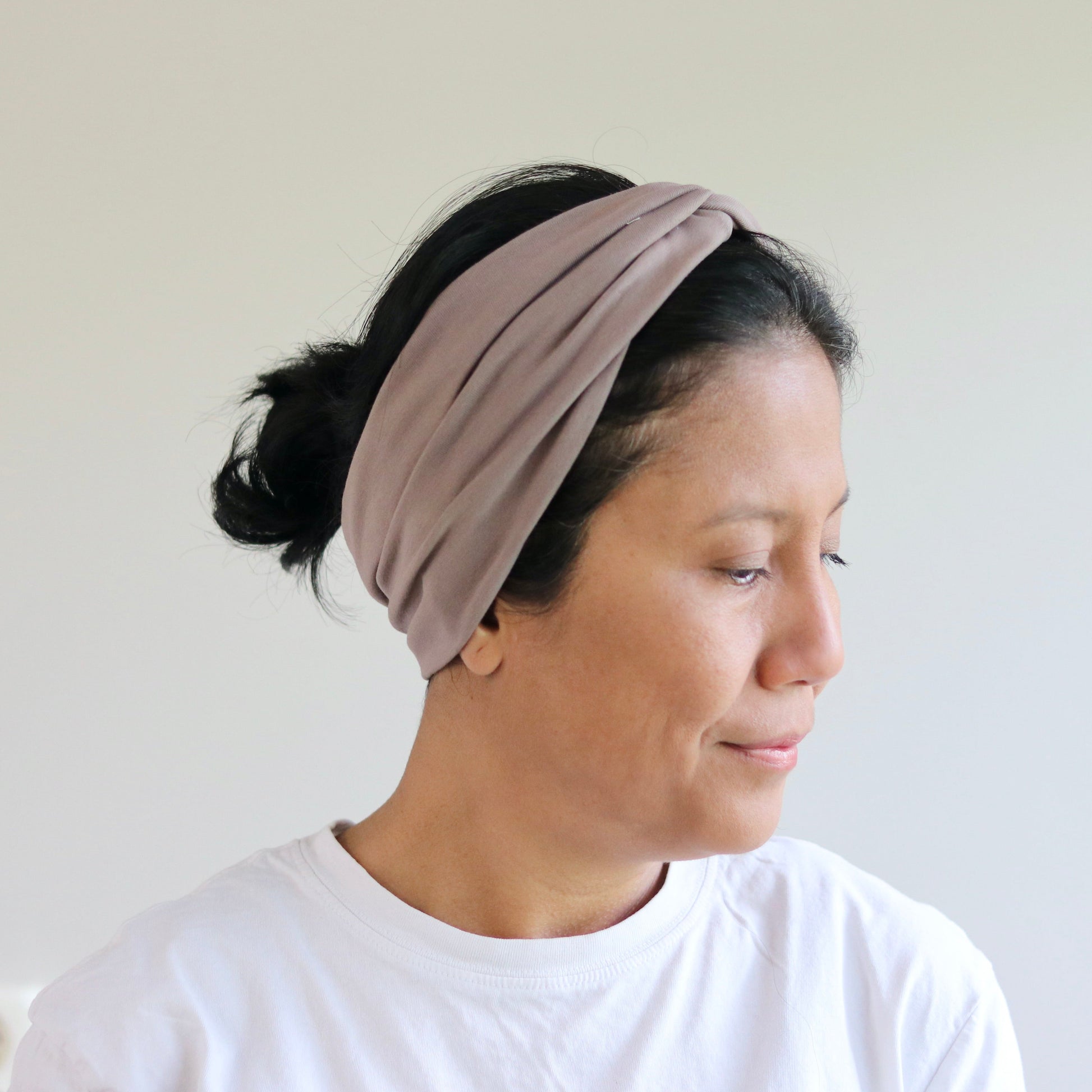 Woman wearing a beige headband against a plain background