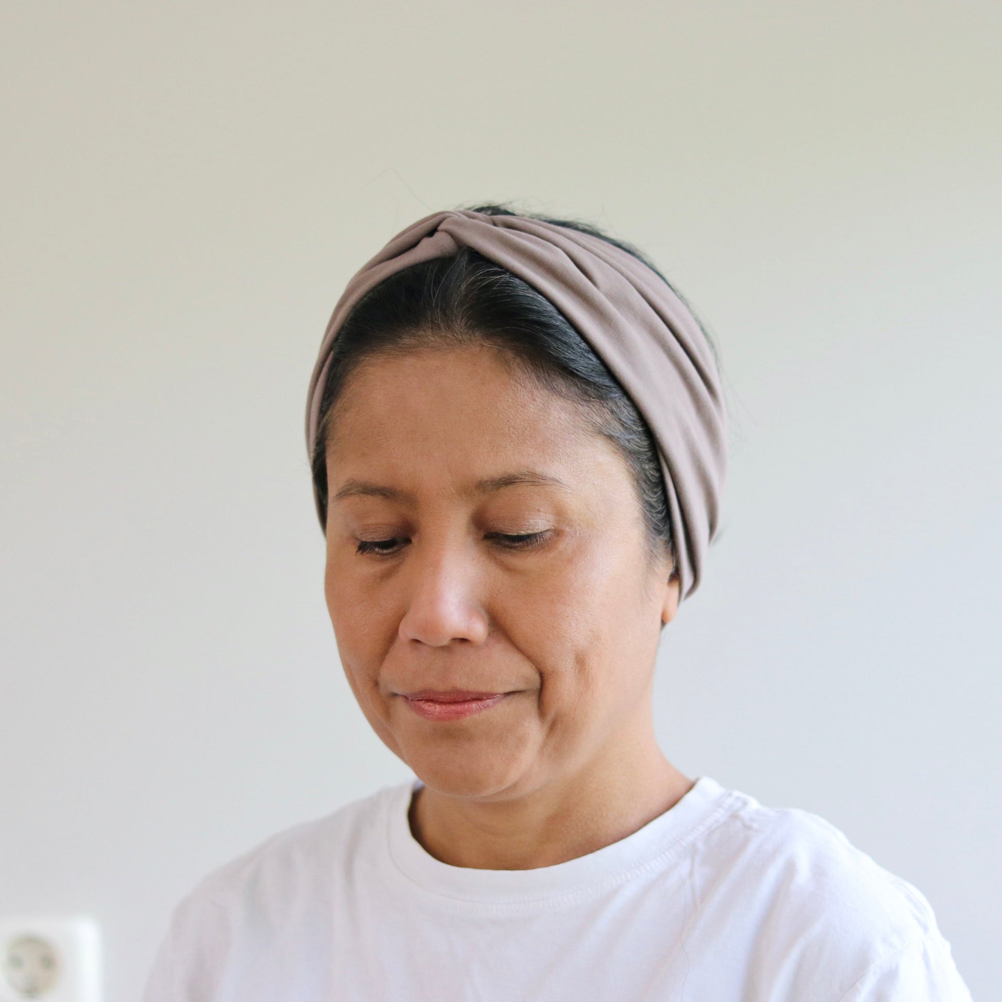 Woman wearing a headscarf and white shirt against a plain background