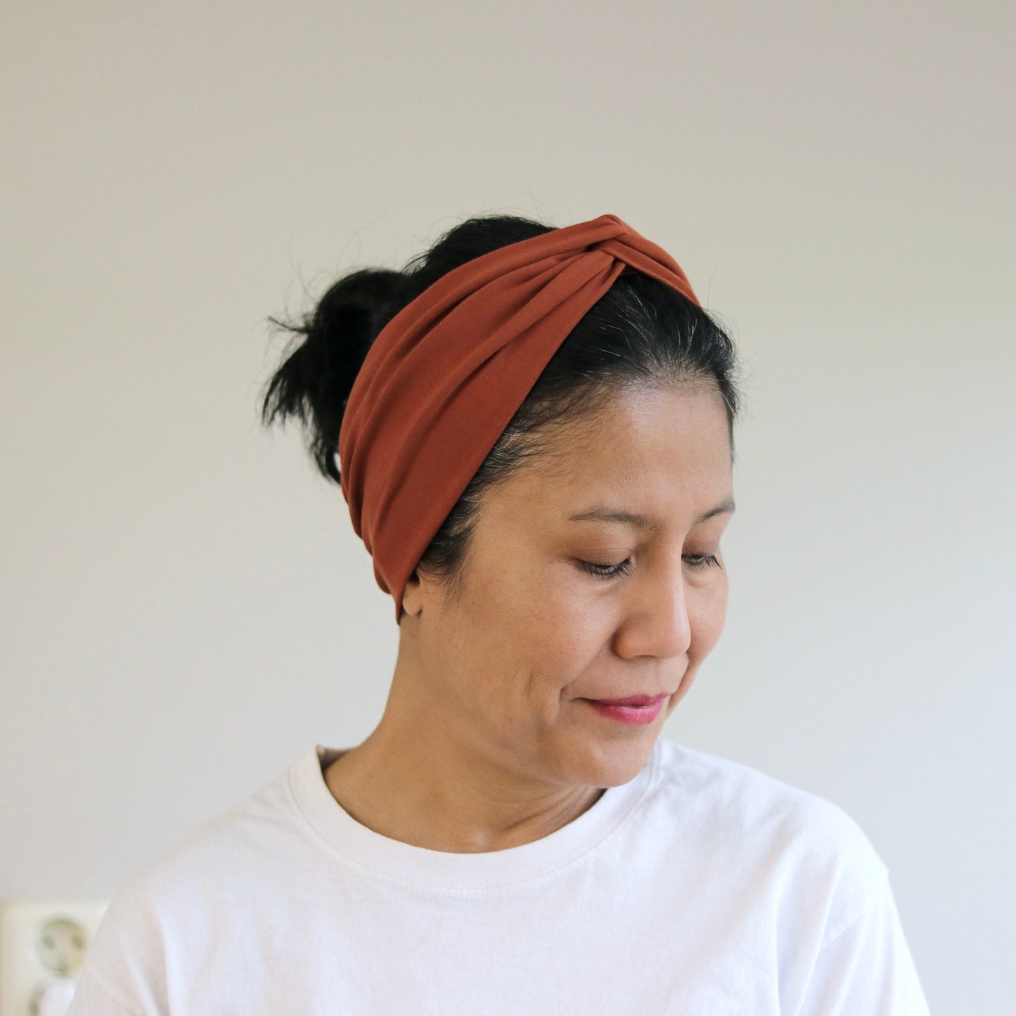 Woman wearing a rust brown headband against a plain background