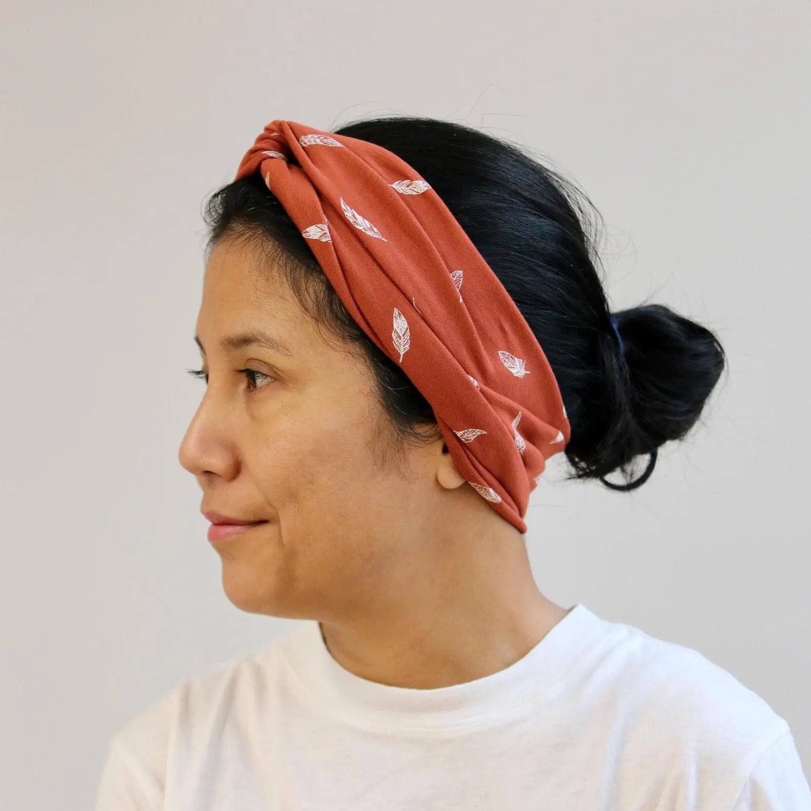 Person wearing a rust-colored headband with feather pattern on a plain background