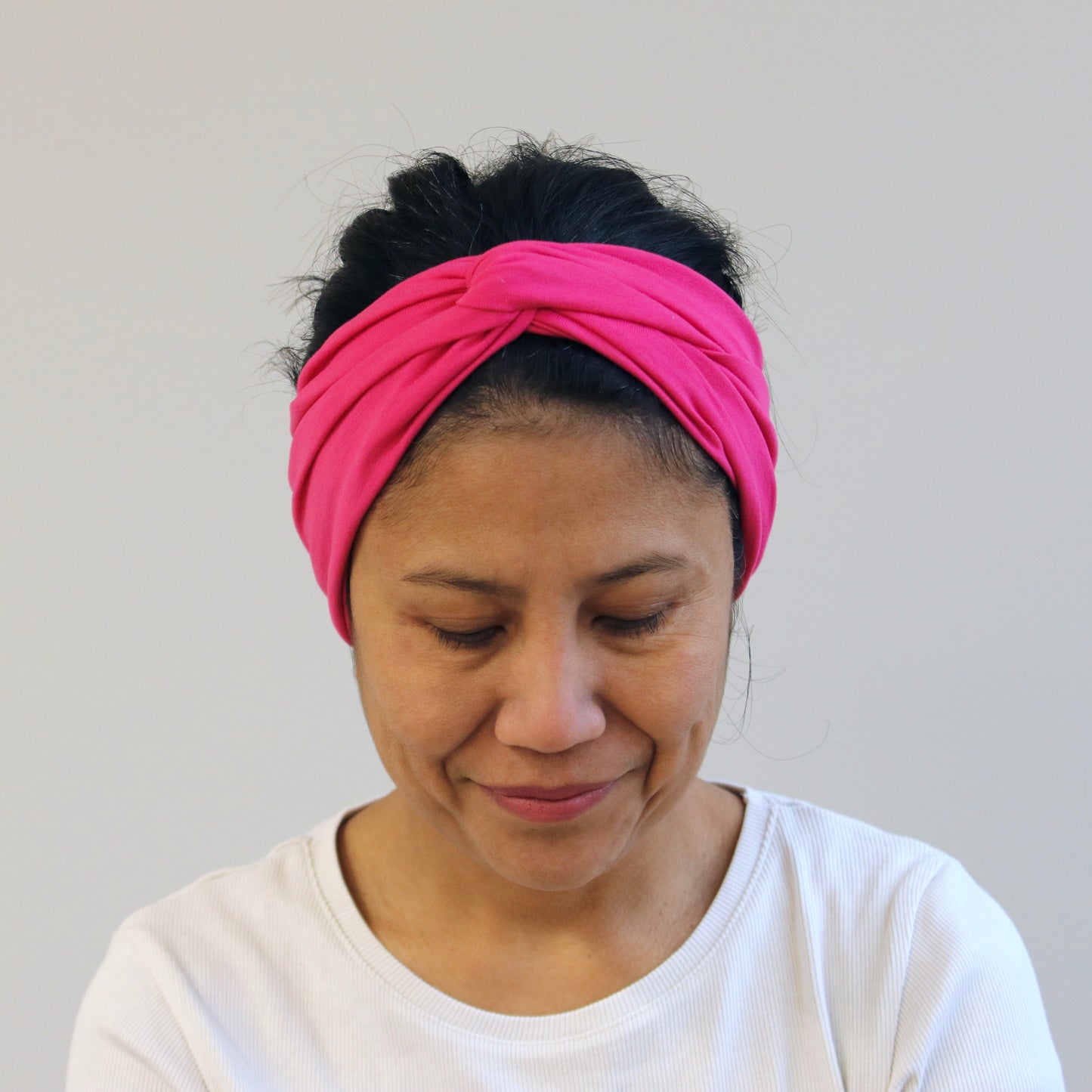 Woman wearing a fuchsia- pink headband against a plain background