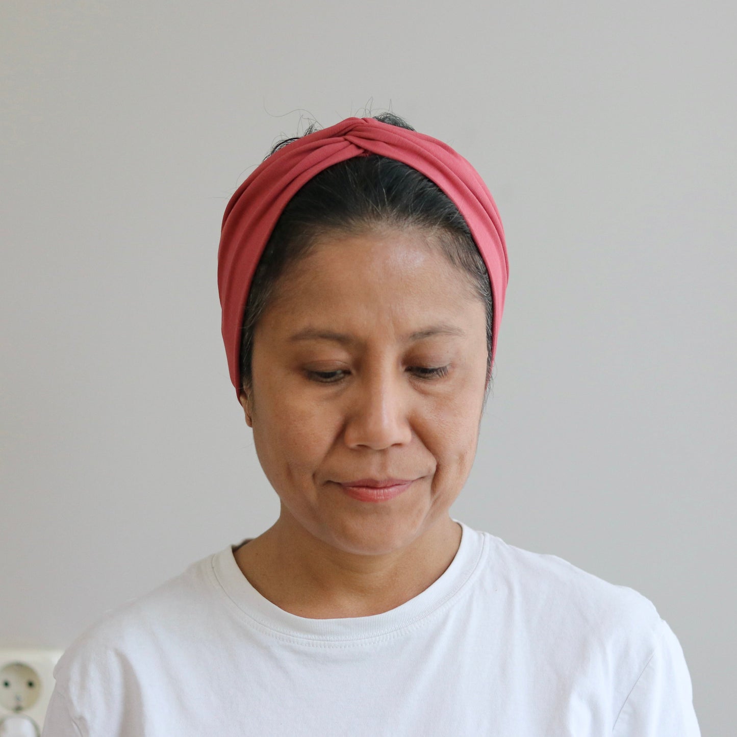 Woman wearing a pink headband and white shirt against a plain background