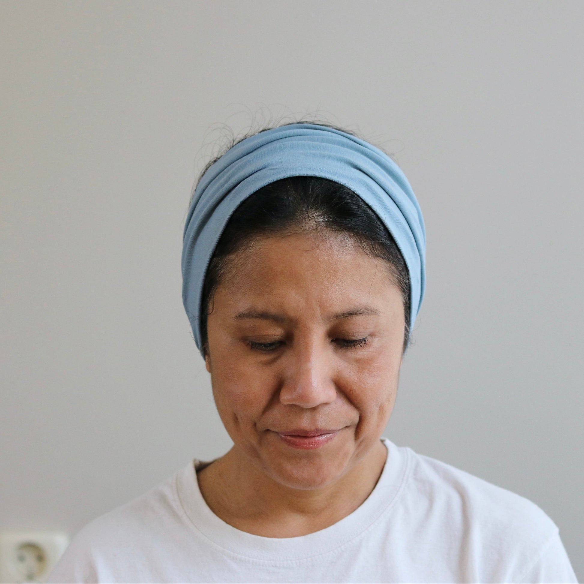 Woman wearing a blue headscarf and white shirt against a plain background