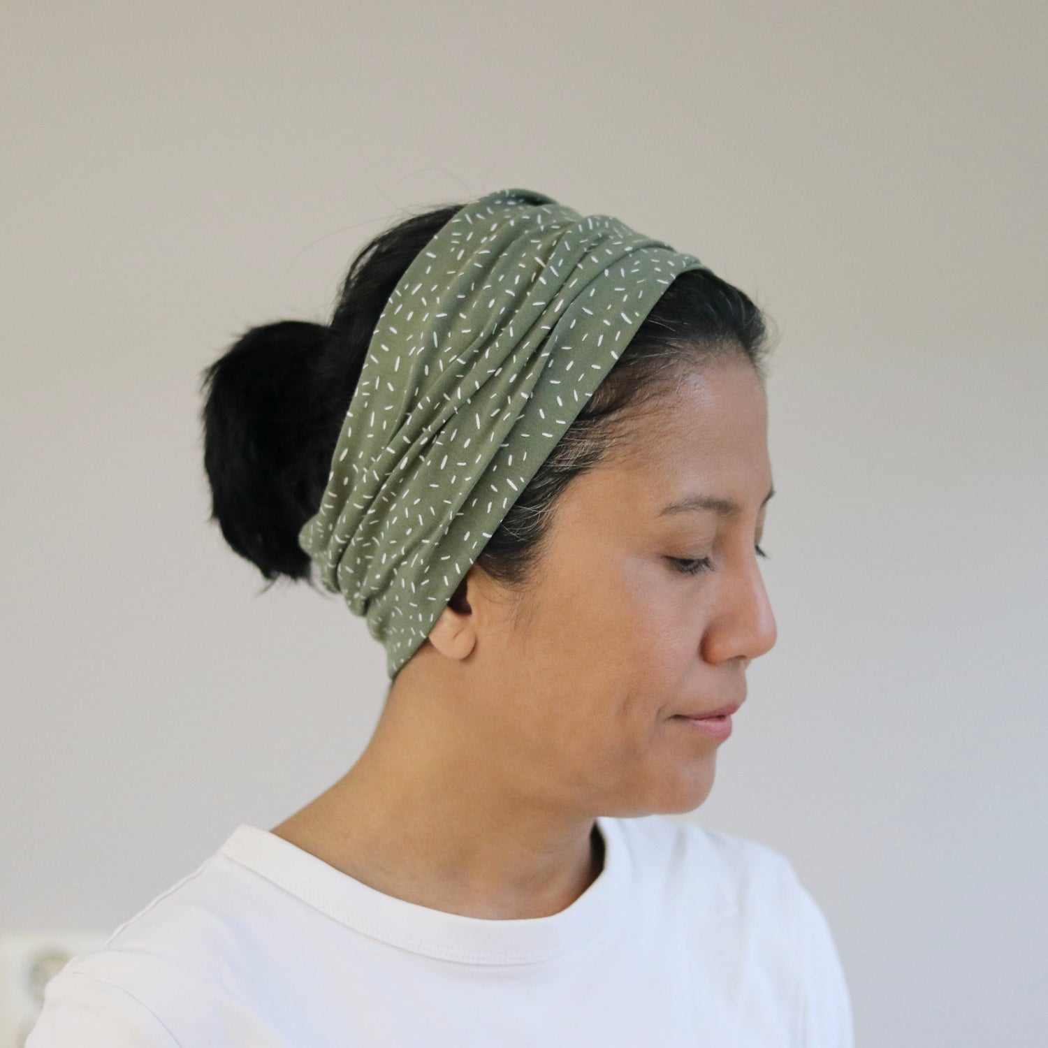 Woman wearing a green headband with white patterns against a plain background