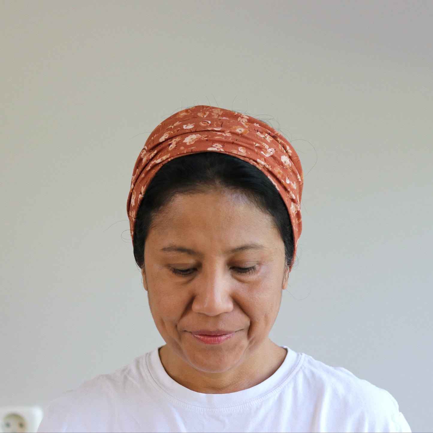 Woman wearing a patterned headscarf and white shirt against a plain background