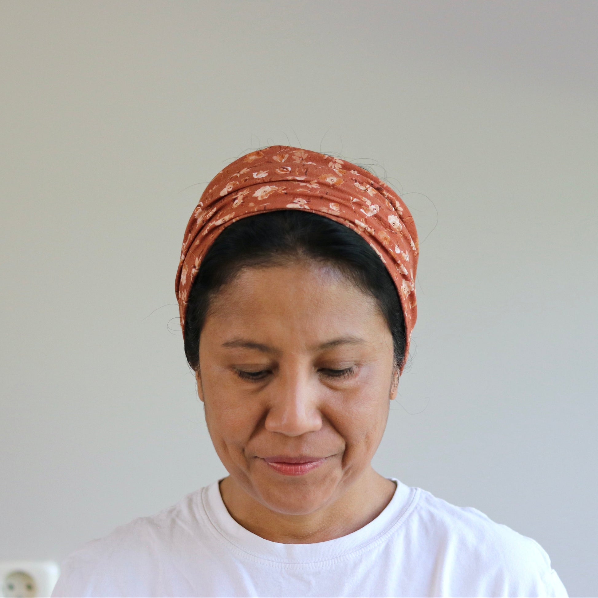 Woman wearing a patterned headscarf and white shirt against a plain background