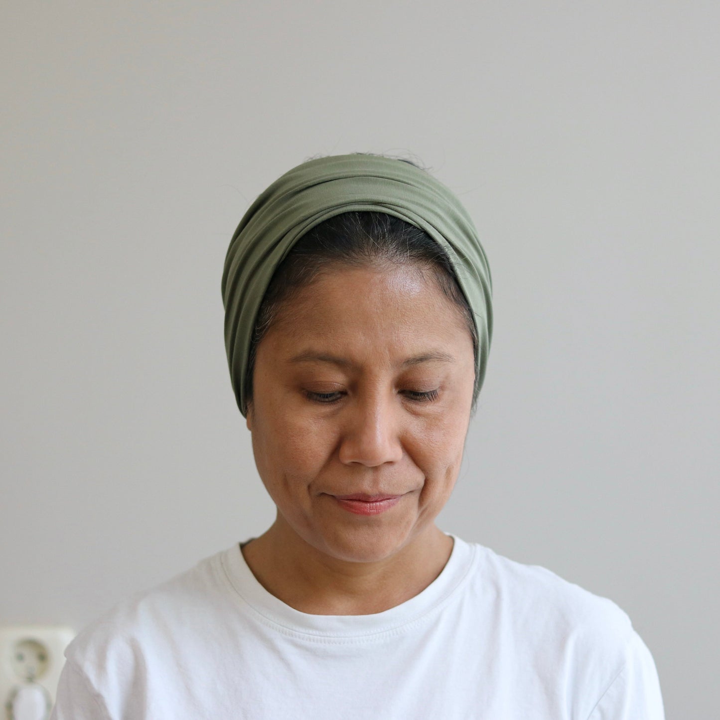 Woman wearing a green headscarf and white shirt against a plain background