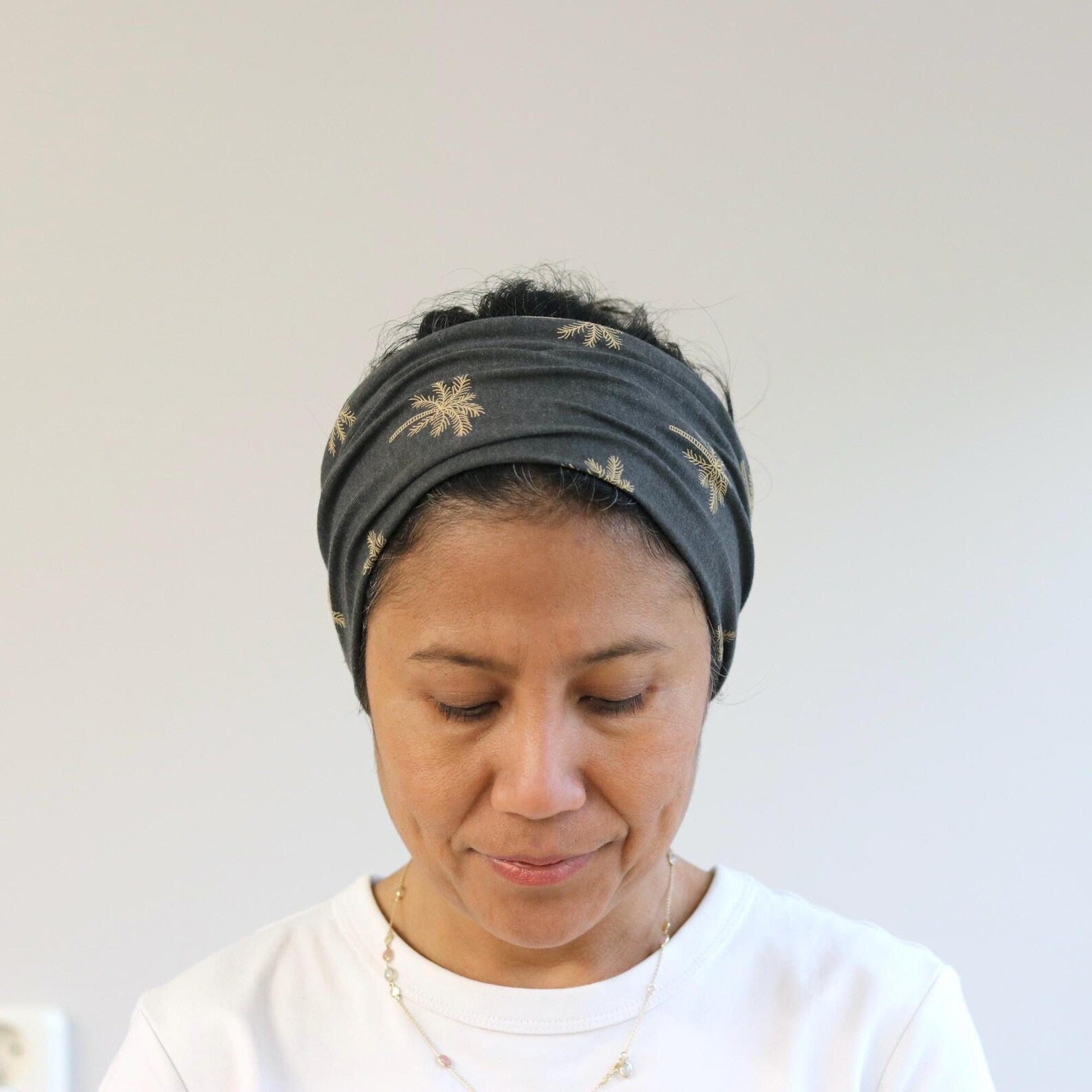 Woman wearing a gray headband with gold patterns against a plain background