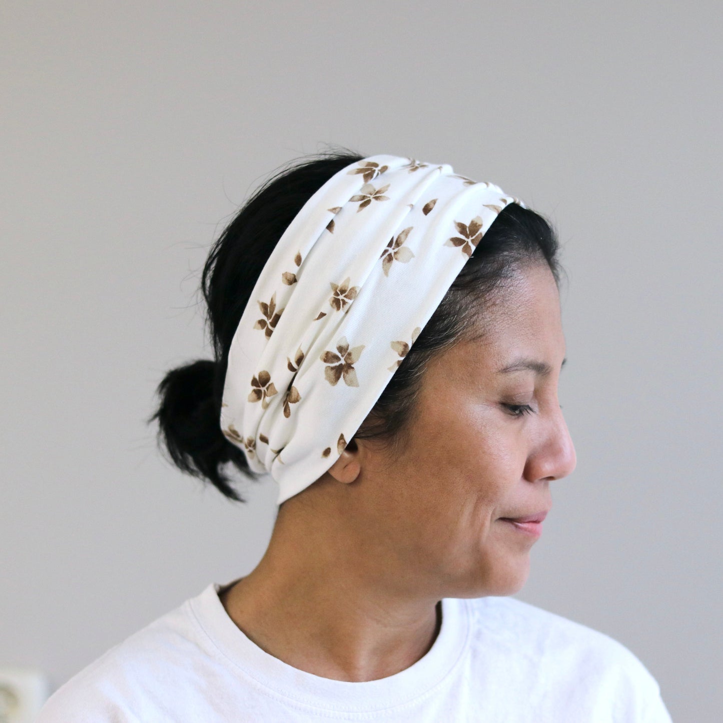 Woman wearing a white headband with brown floral pattern against a plain background