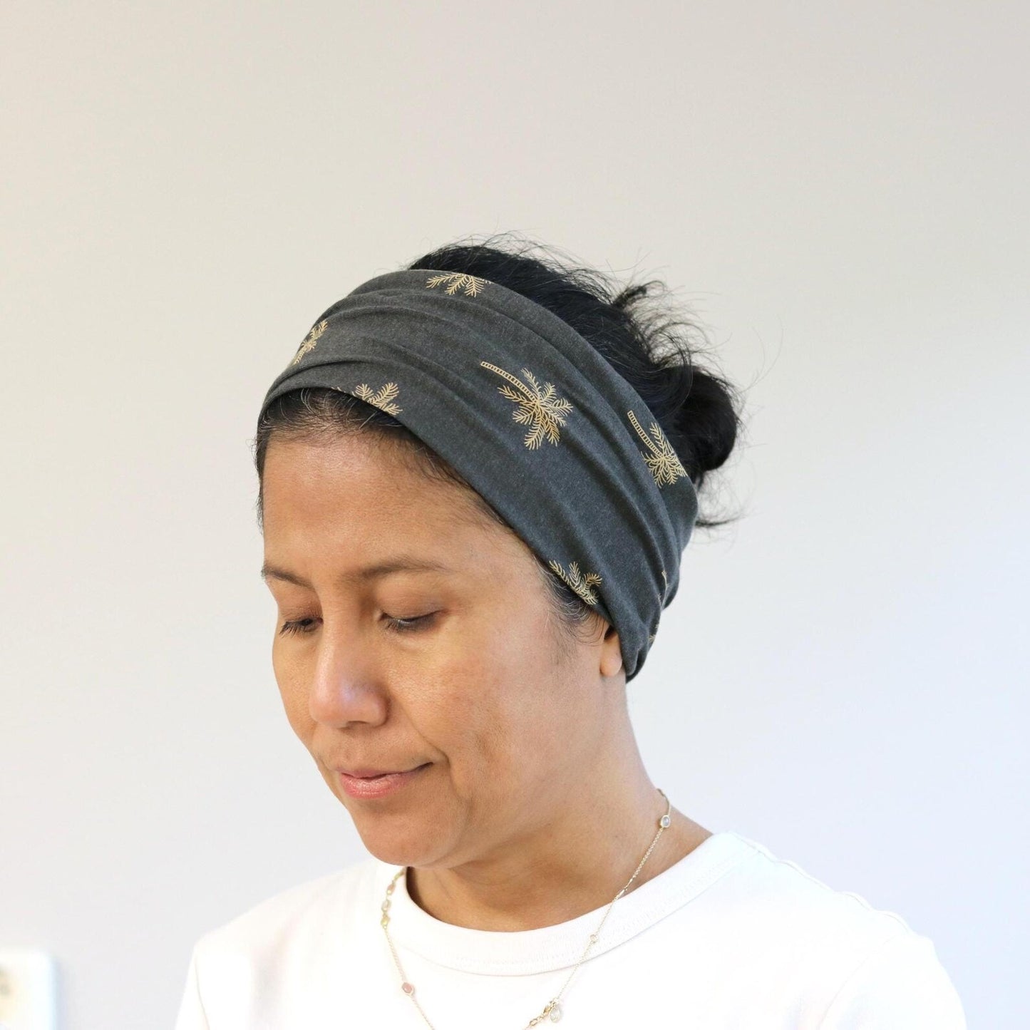 Woman wearing a dark gray headband with gold patterns on a white background