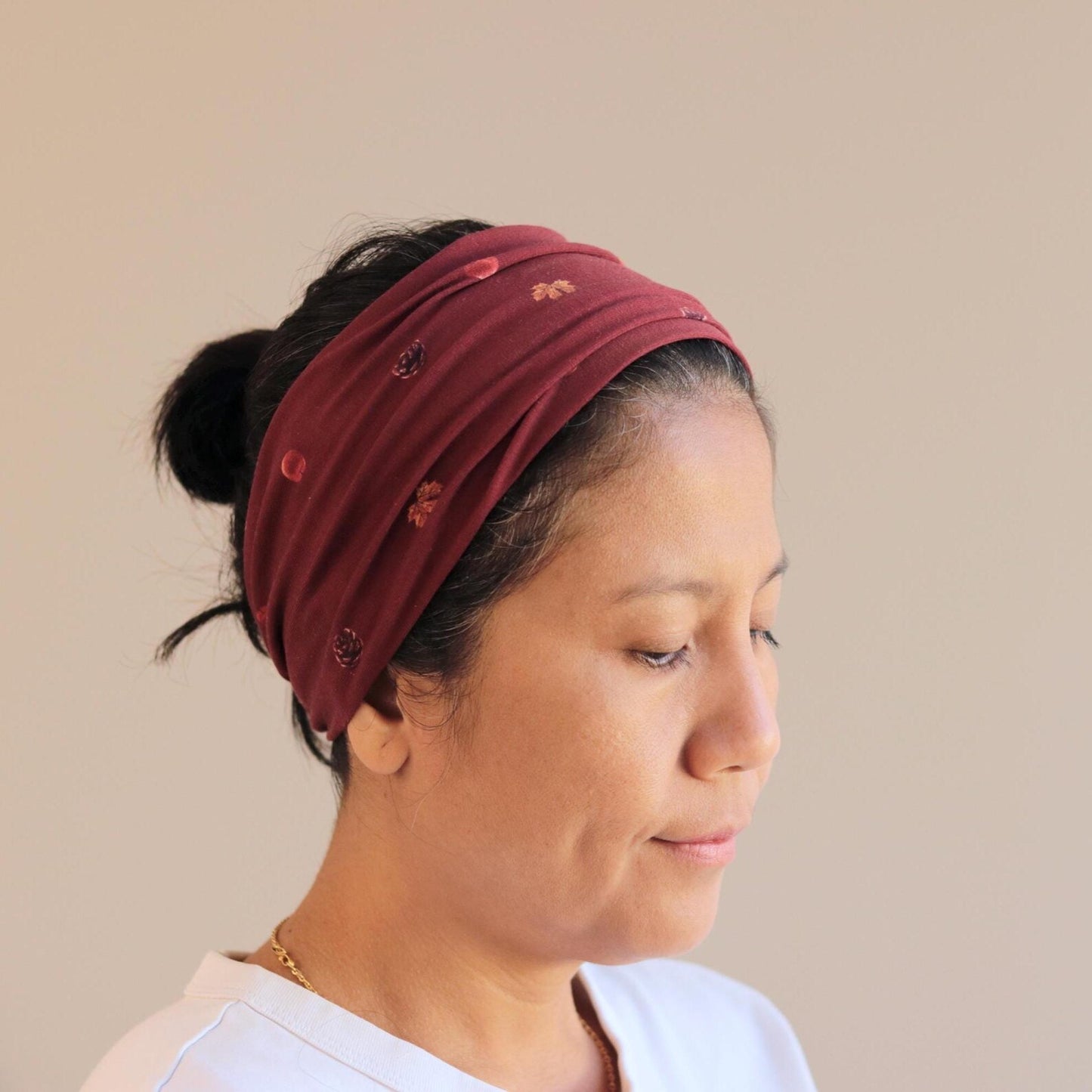 Woman wearing a burgundy headband with small embellishments on a beige background