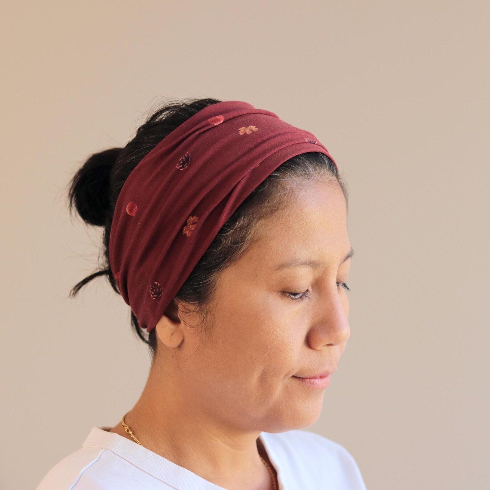 Woman wearing a burgundy headband with small embellishments on a beige background