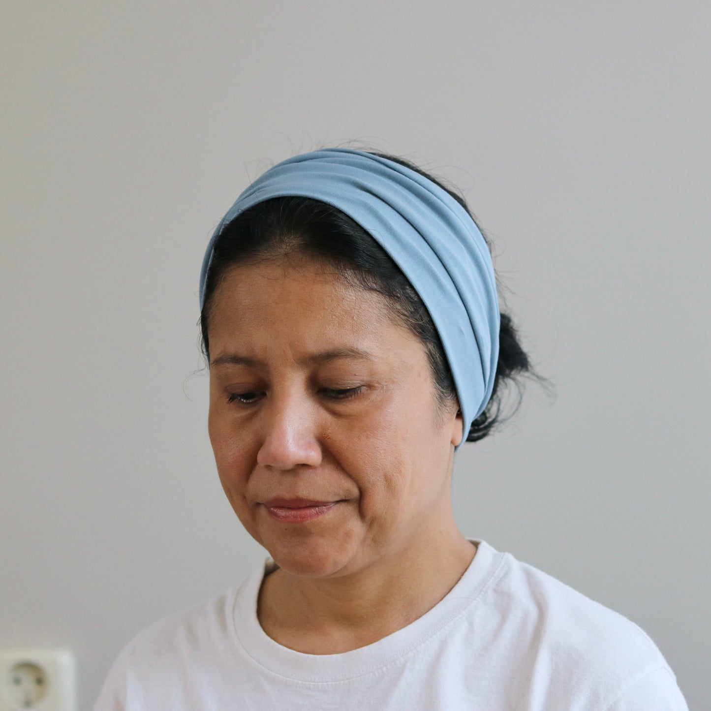 Woman wearing a blue headscarf and white shirt against a plain background
