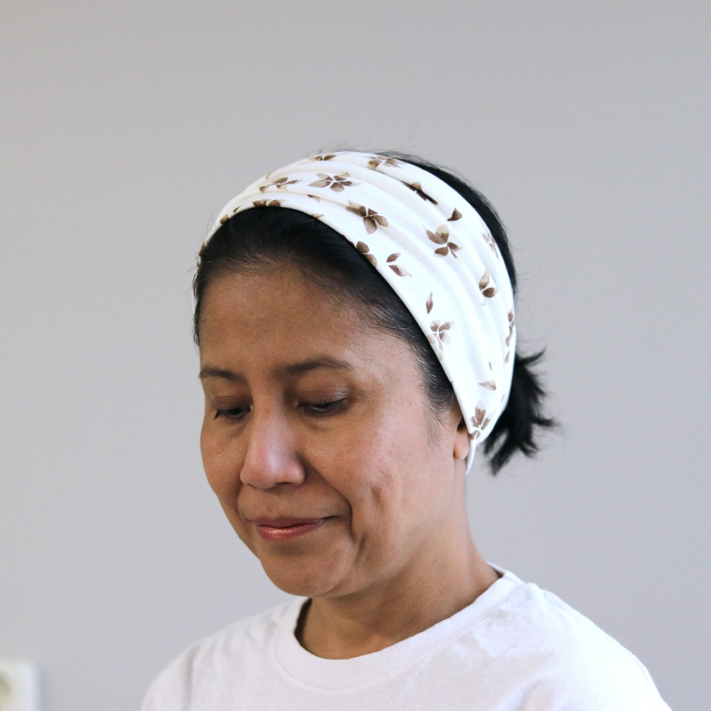 Woman wearing a white headscarf with a pattern against a plain background